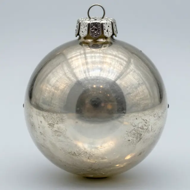 A close-up macro view of a worn vintage silver mercury glass Christmas ornament against a plain light gray background.