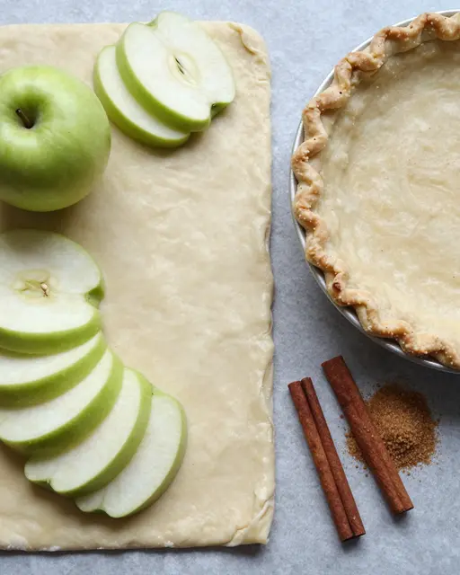 Top-down flat lay of raw pie ingredients arranged on parchment paper for apple pie baking.