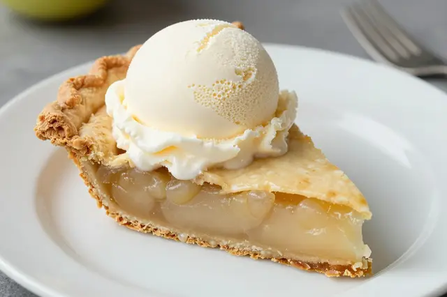 A slice of apple pie topped with a scoop of vanilla ice cream sits on a white ceramic plate.