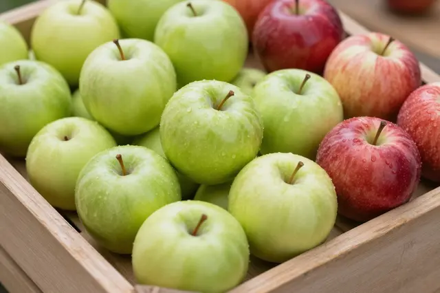Green and red glossy apples dotted with water droplets fill a slatted wooden harvest crate.