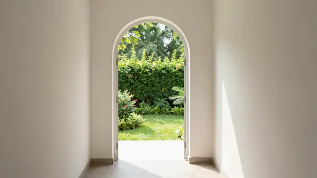 Sunlit interior hallway with a white arched doorway opening onto a lush green garden