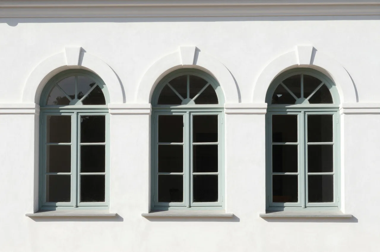 Three matching arched windows with pale green frames set in a smooth white stucco building facade