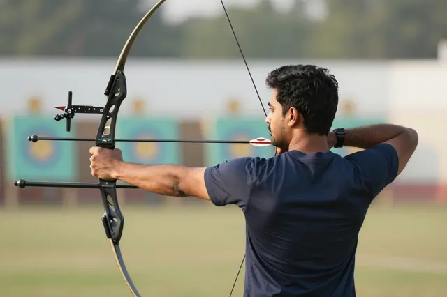 South Asian male archer drawing and aiming a recurve bow at outdoor archery range targets in soft morning light
