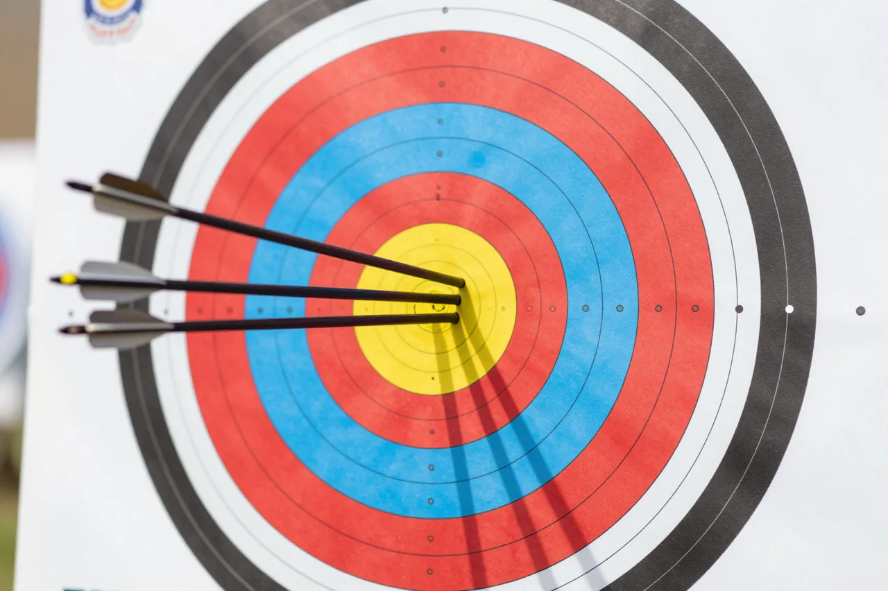 Three arrows embedded in the yellow bullseye of a standard colored archery target
