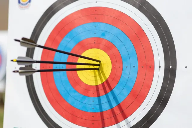Three arrows embedded in the yellow bullseye of a standard colored archery target