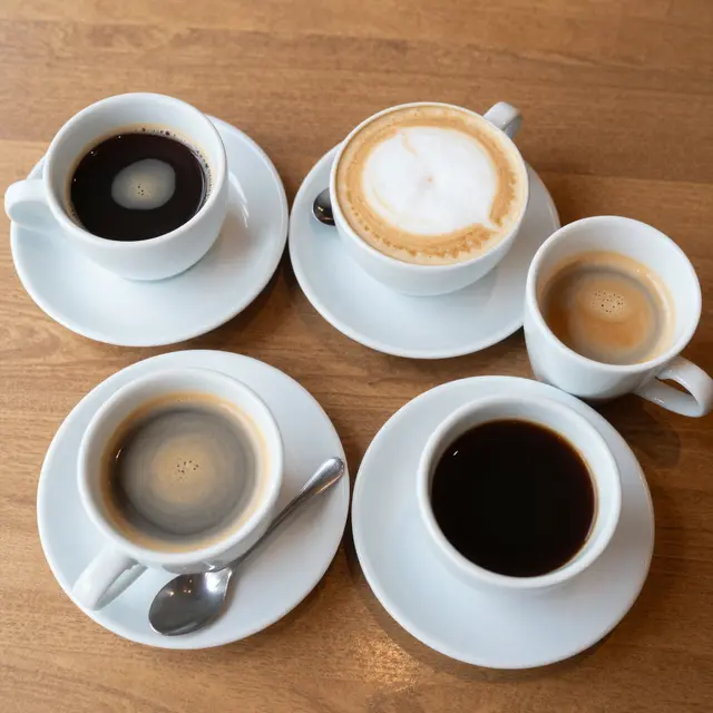 Top down view of five white ceramic coffee cups with different brews arranged on a light wooden table