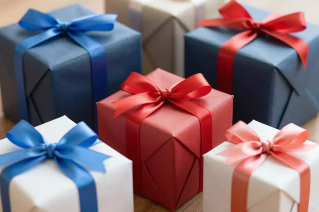Wrapped gift boxes of varying sizes with colorful satin ribbons rest on a wooden surface