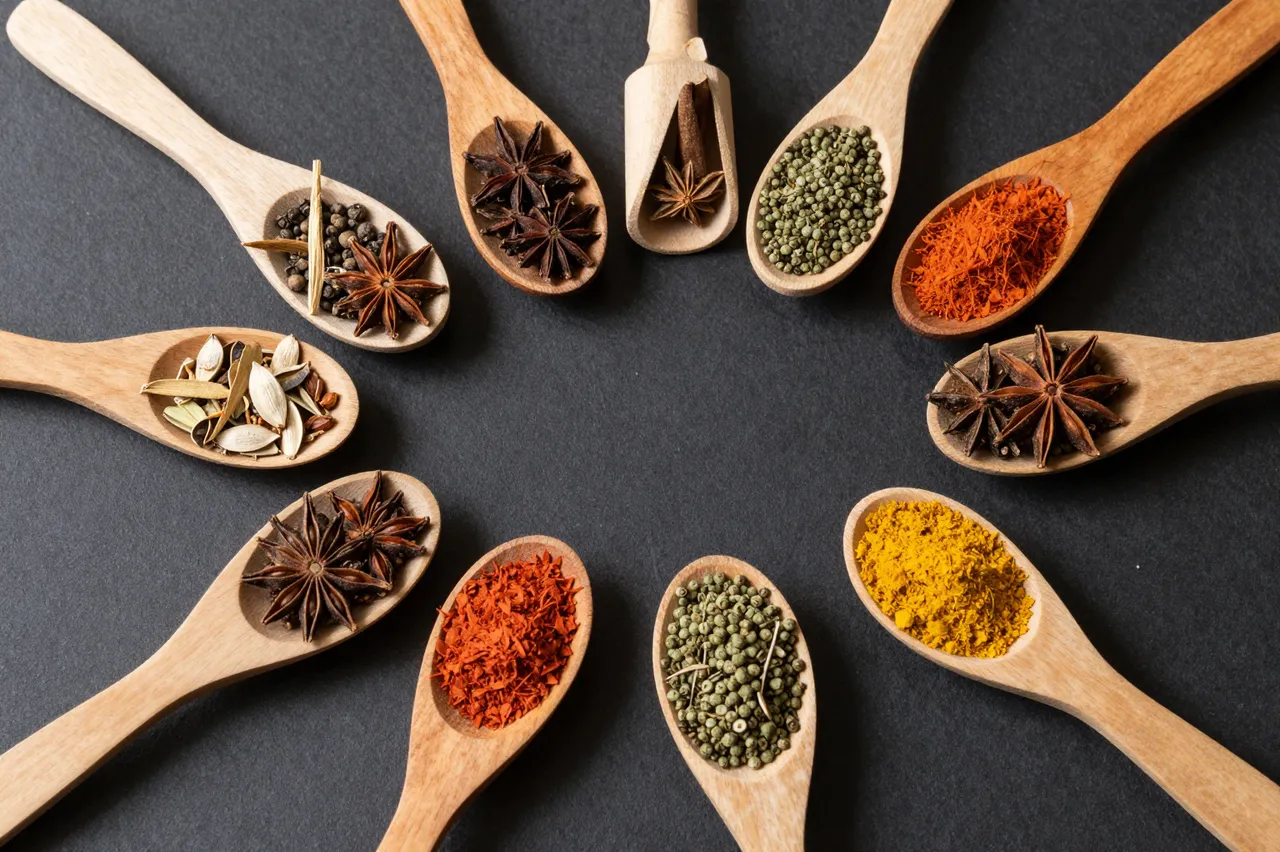 Arranged wooden spoons holding varied colorful spices on a dark flat lay background
