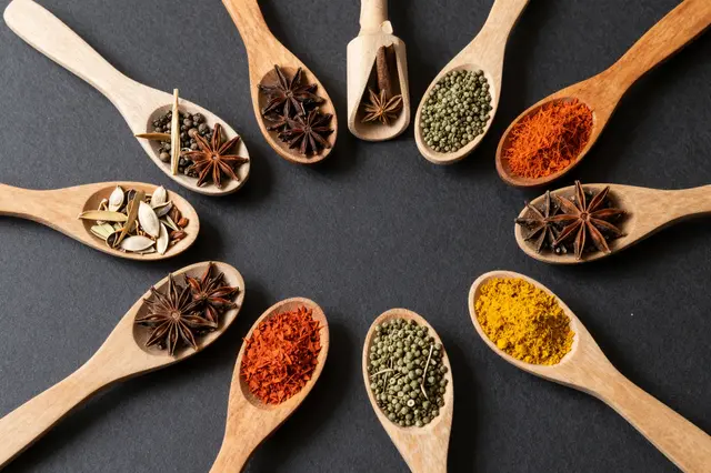 Arranged wooden spoons holding varied colorful spices on a dark flat lay background