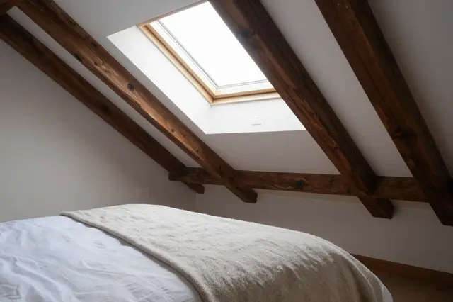 Cozy attic guest bedroom with dark timber rafters, a skylight above a bed topped with a wool throw