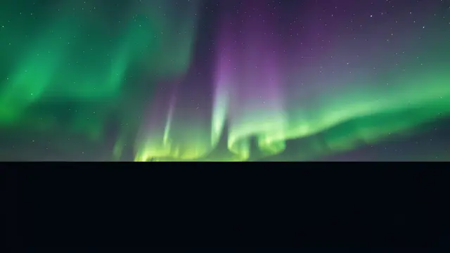 Green and violet aurora curtains glow above a dark empty lower section of starry night sky