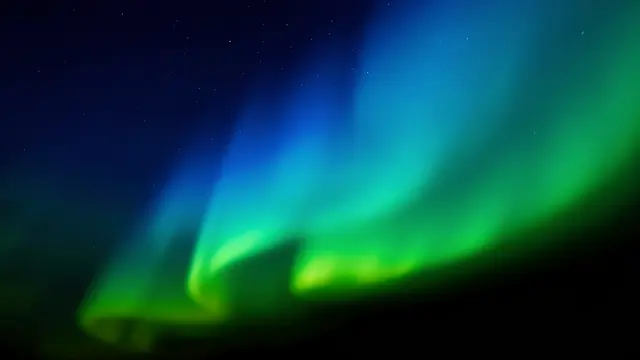 Soft blurred blue and green aurora bands arc across a dark star-dusted night sky