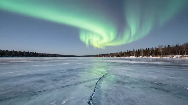 Swirling green aurora arcs above a frozen cracked ice lake lined with winter forest