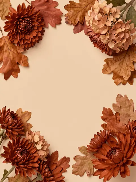 Rust chrysanthemums, dried hydrangea and oak leaves arranged in a corner frame around empty warm beige copy space