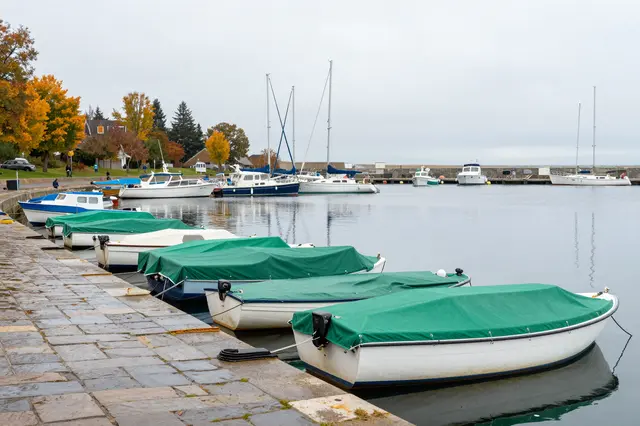 Covered small boats line a stone harbor slipway under a drizzly gray autumn sky