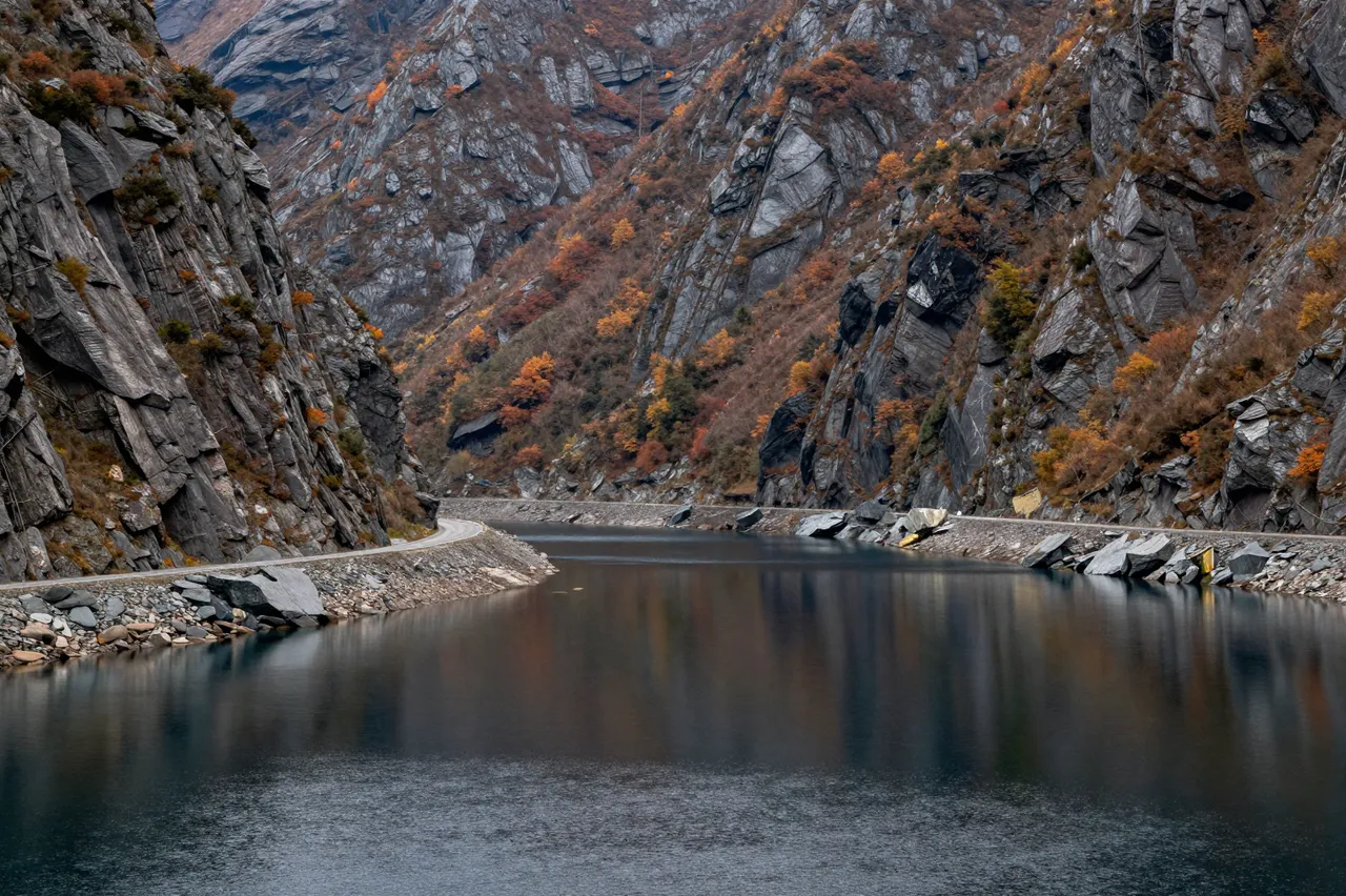 Winding road runs along calm reflective inlet water between steep rocky autumn mountains
