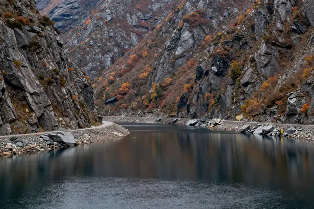 Winding road runs along calm reflective inlet water between steep rocky autumn mountains