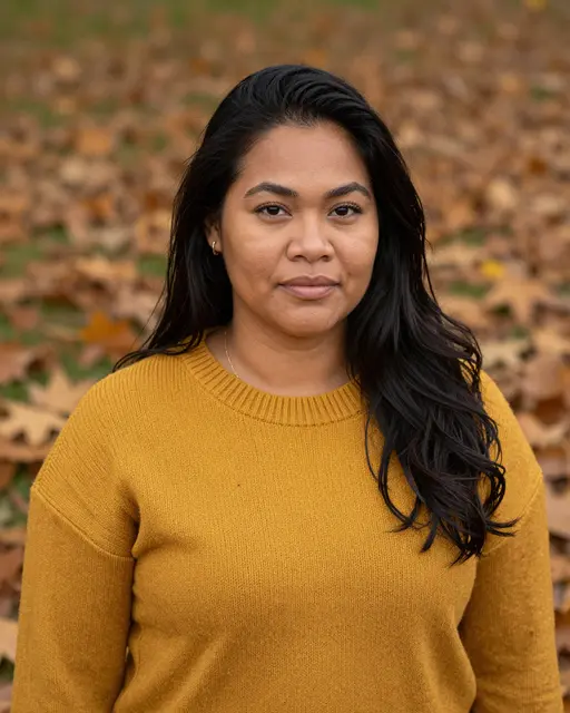 Portrait of a woman in a mustard knit sweater standing in autumn fallen leaves in soft light