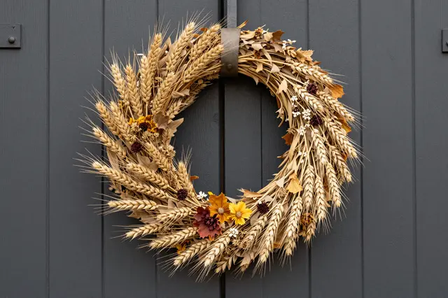 A dried autumn wreath of wheat and fall botanicals hangs on a dark gray paneled barn door