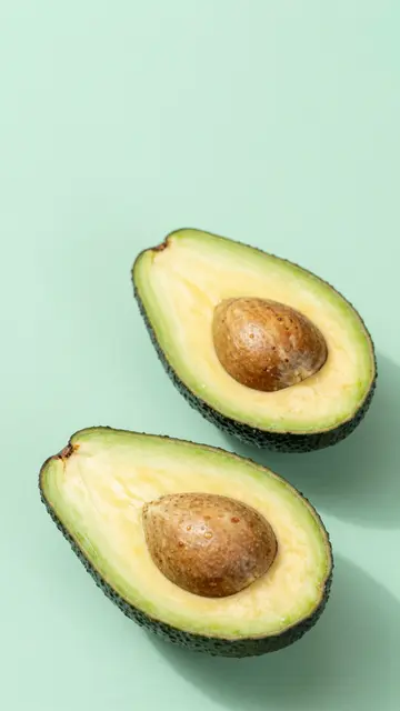 Two halved avocados with intact pits rest on a solid pale mint green background