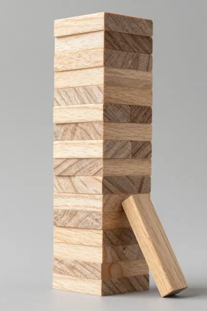 Tall stacked wooden block tower with one displaced leaning block against a plain gray background