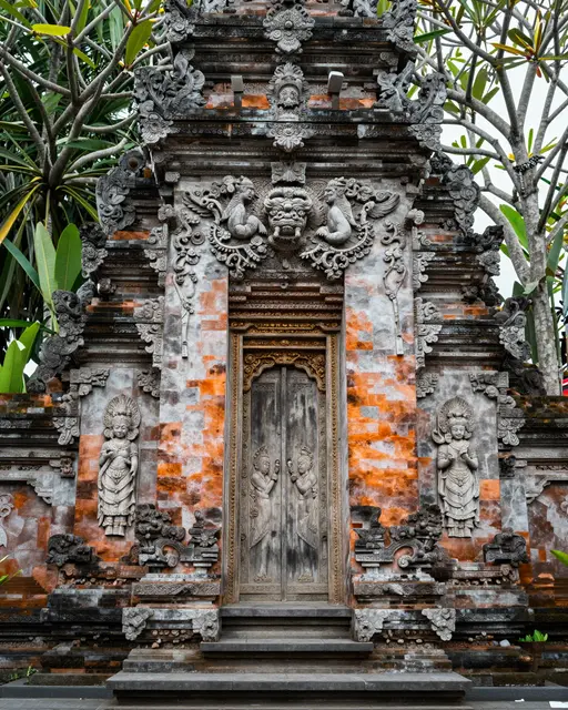 Ornately carved weathered Balinese temple gate flanked by frangipani tree branches