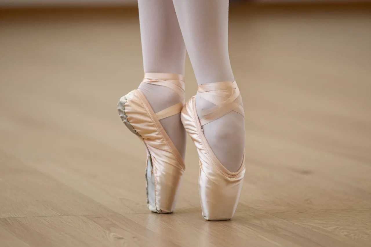 Close-up of a ballet dancer's feet in pointe shoes standing on a wooden dance studio floor