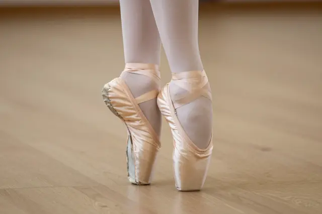 Close-up of a ballet dancer's feet in pointe shoes standing on a wooden dance studio floor
