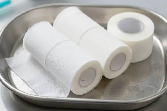 Top view of white gauze bandage and surgical tape rolls resting on a stainless steel medical tray.