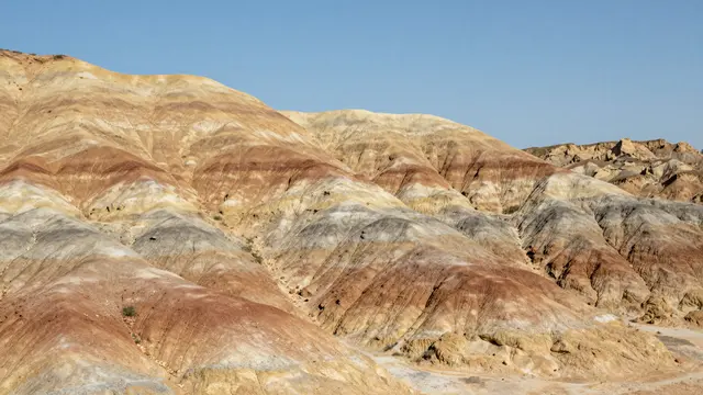 Layered eroded clay hills with rust, cream and gray bands rise under a clear blue sky