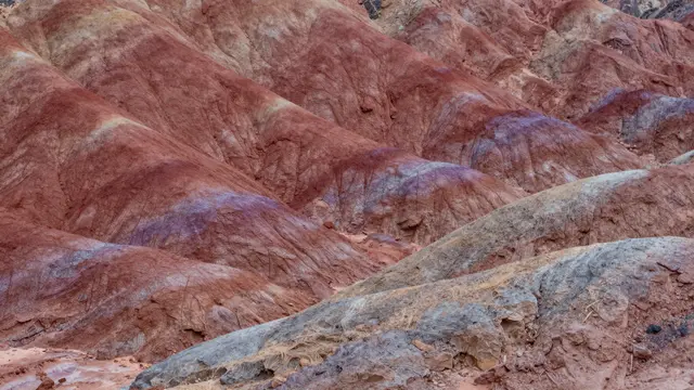 Textured eroded clay hills show distinct horizontal bands of red, purple, and gray sedimentary layers