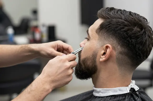 A barber uses scissors to trim the beard of a seated customer in a barbershop