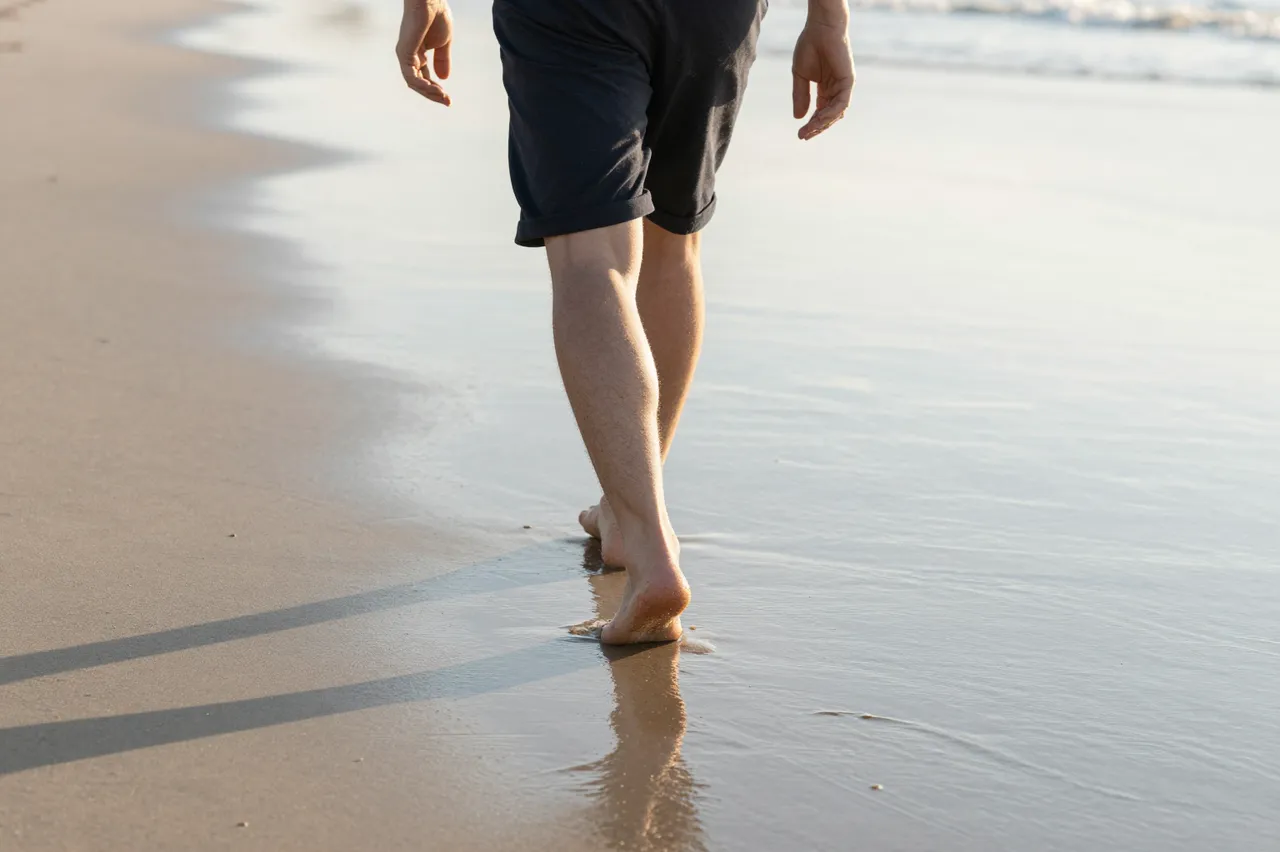 Back view of an adult walking barefoot along wet sand at the beach at sunrise, only the legs, hands and lower torso are