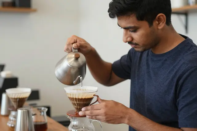 South Asian barista pouring water from a gooseneck kettle over a pour-over coffee dripper