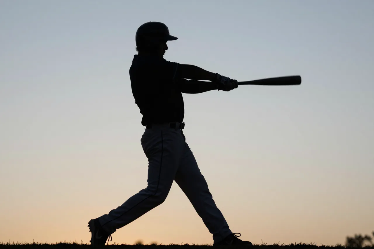 Silhouette of a baseball batter mid-swing against a soft gradient dusk sky