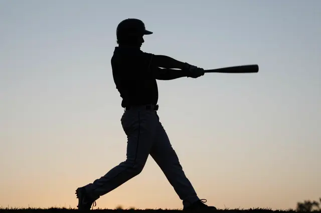 Silhouette of a baseball batter mid-swing against a soft gradient dusk sky
