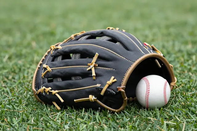 A black leather baseball glove rests on green grass with a white baseball tucked inside its opening.
