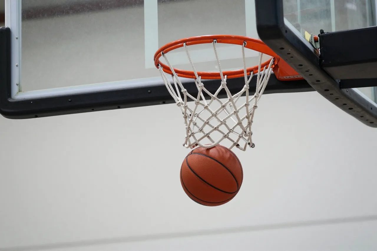 A basketball passes through the net of an outdoor basketball hoop in a mid-shot moment.