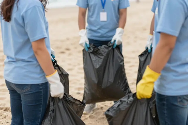 Group of beach cleanup volunteers holding black trash sacks while standing on a sandy shore