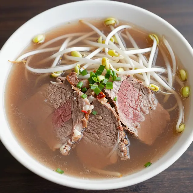 Top down view of a bowl of beef pho with rare steak, bean sprouts, and chopped green onion in savory broth.