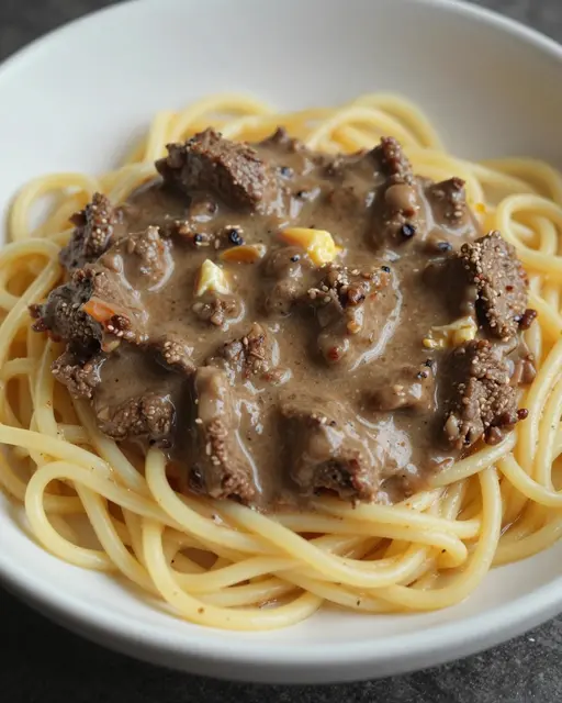 Close-up view of creamy beef stroganoff served over thick egg noodles in a white bowl