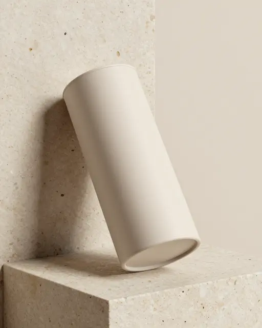 A plain soft beige cylindrical container rests on a textured travertine stone block against a neutral beige background