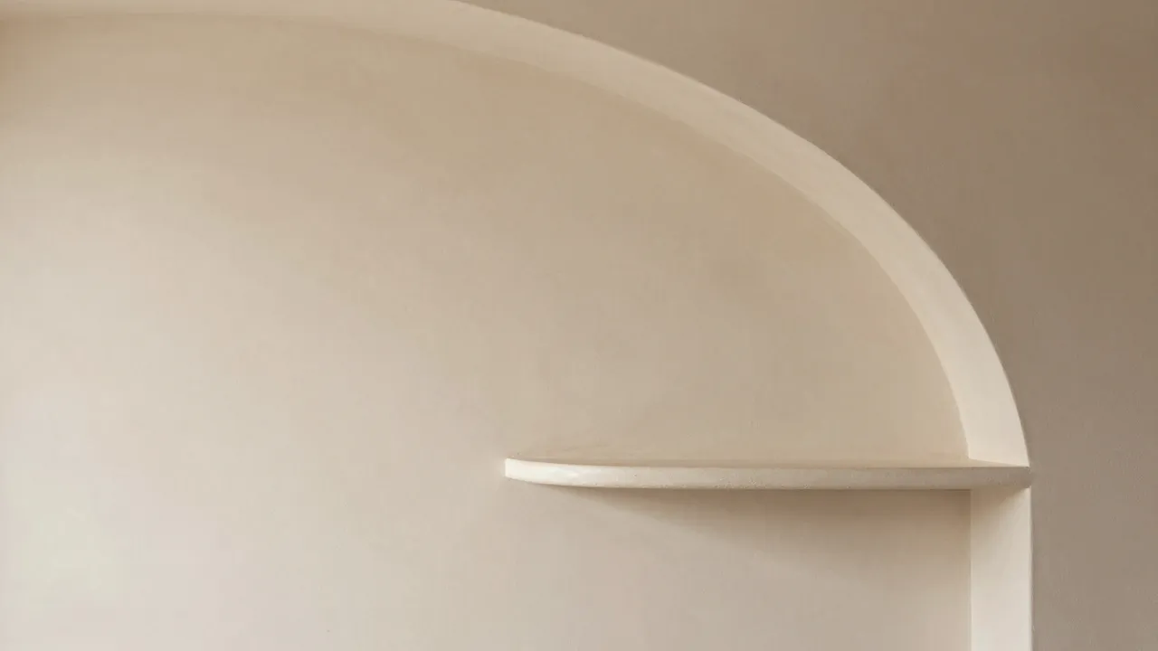 A smooth matte beige plaster wall features a curved built-in shelf on the right with empty copy space on the left.