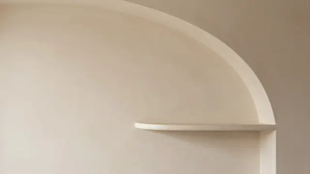 A smooth matte beige plaster wall features a curved built-in shelf on the right with empty copy space on the left.