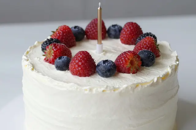 White frosted birthday cake topped with fresh mixed berries and a single gold candle.
