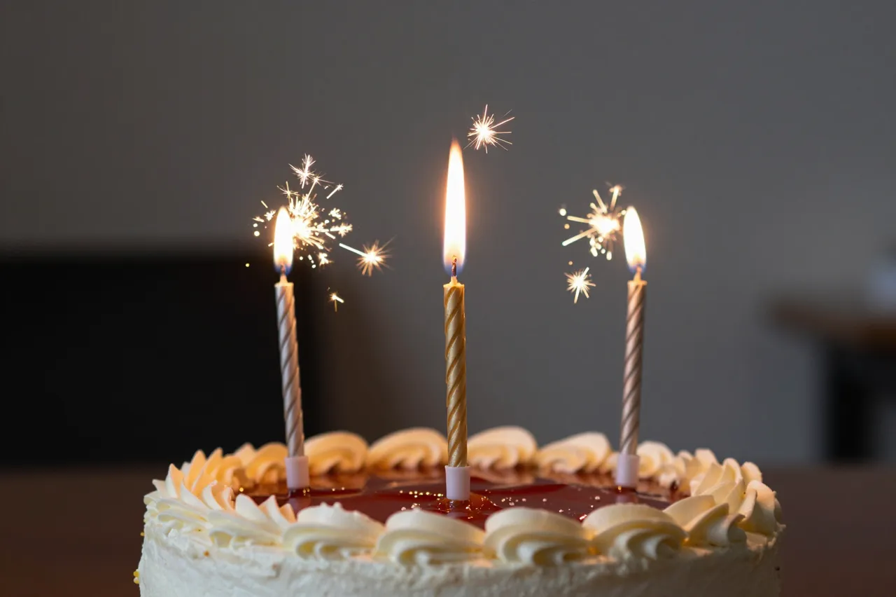 Frosted birthday cake holds lit candles and sparklers against a dark blurred room background