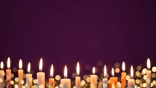 Lit birthday candles and soft gold bokeh sit along the bottom of a deep plum background with empty upper copy space