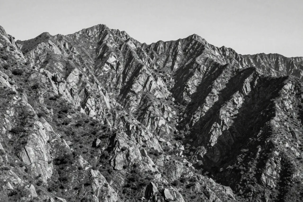 Black and white view of a rugged, craggy mountain range under a pale clear sky