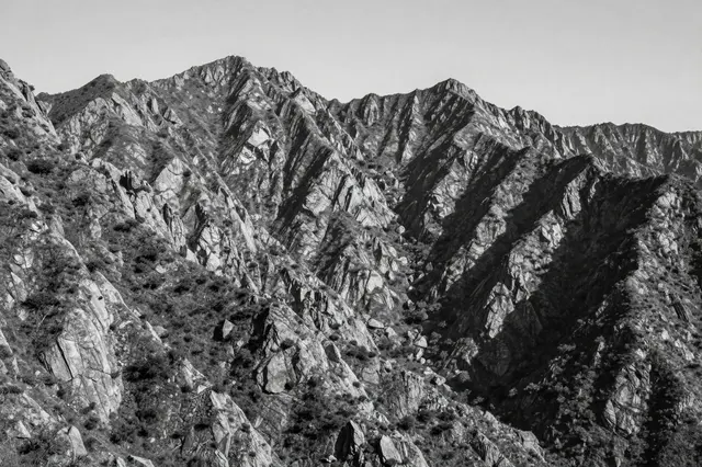 Black and white view of a rugged, craggy mountain range under a pale clear sky