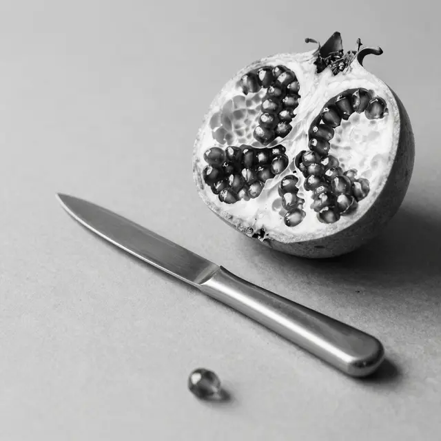 Halved glistening pomegranate rests beside a metal paring knife on a smooth neutral surface